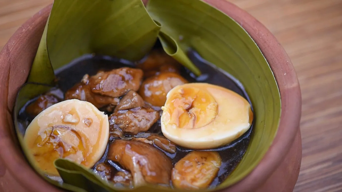 Braised pork adobo with halved boiled eggs in a clay pot lined with banana leaf