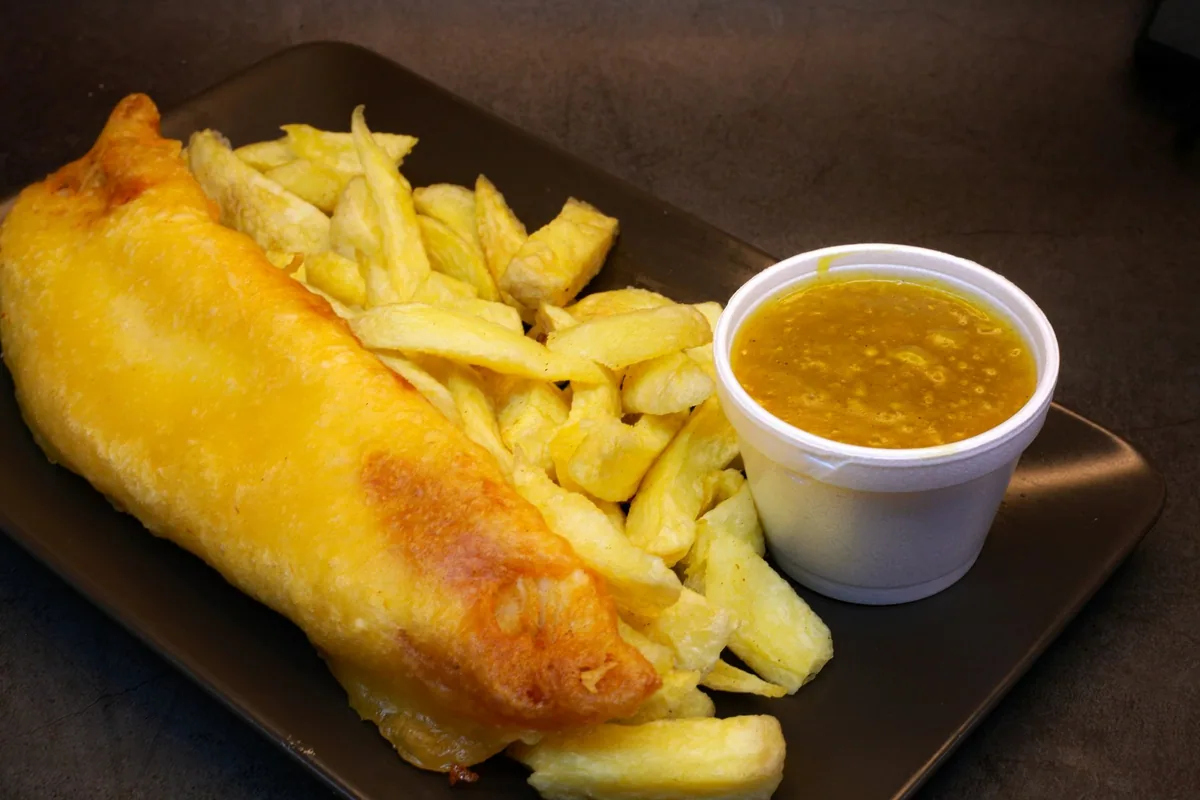 Battered fish with thick-cut chips and a tub of curry sauce served on a tray