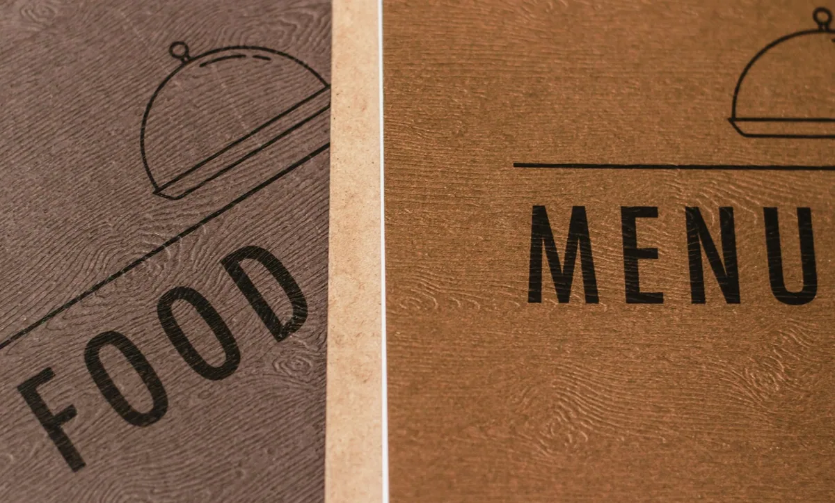 Two textured card menu covers printed with the words FOOD and MENU under a line drawing of a cloche