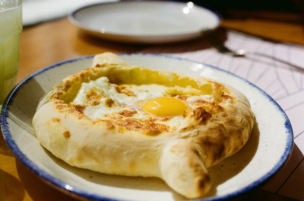 Adjarian khachapuri, a boat-shaped cheese bread with a soft egg yolk in the middle, on a rimmed plate