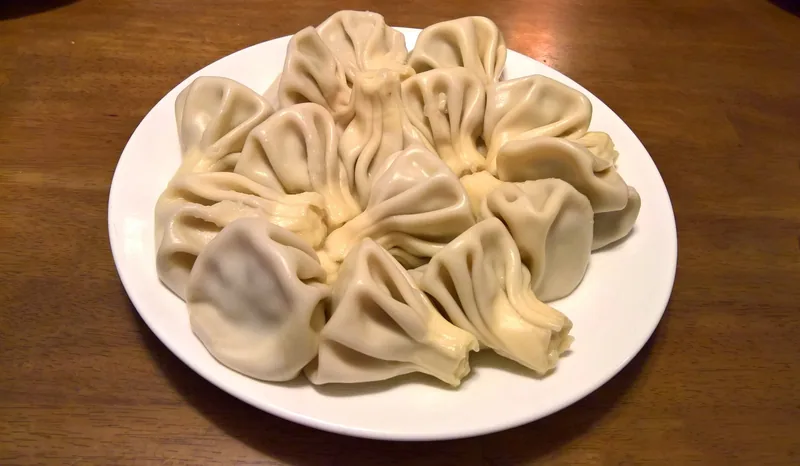 A white plate piled with khinkali, the hand-pleated Georgian meat dumplings, on a dark wooden table