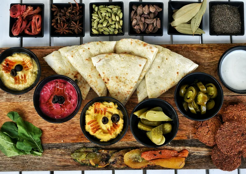 Warm flatbread with bowls of hummus, beetroot dip, pickles and chillies on a wooden board