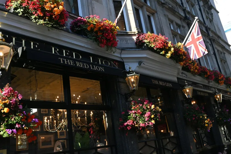 The dark frontage of The Red Lion pub hung with flower baskets, lanterns and a Union flag