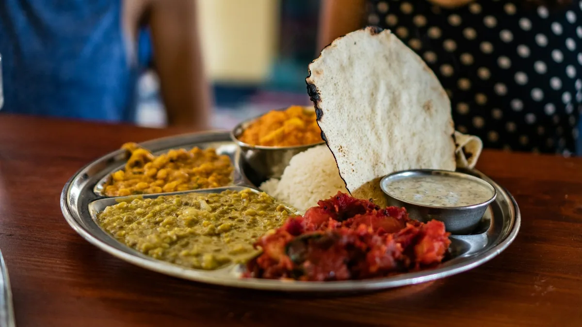 A steel platter of dal and spiced chicken with crisp papadums and flatbread alongside