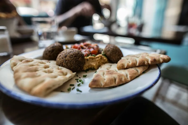 A plate of falafel balls with hummus, chopped tomato salad and torn pita bread on a cafe table