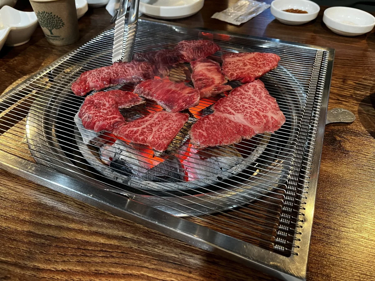 Slices of marbled beef cooking on a round tabletop grill at a Korean barbecue