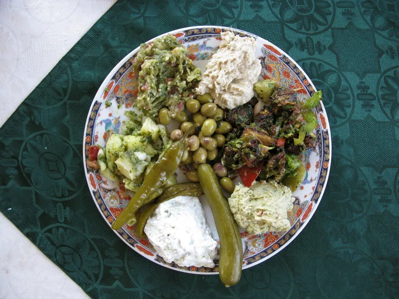 A plate of mezze: hummus, green olives, pickled chillies and cucumber, chopped salads and a yoghurt dip