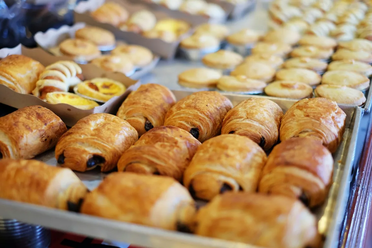 Rows of freshly baked croissants and pains au chocolat lined up in a bakery display case