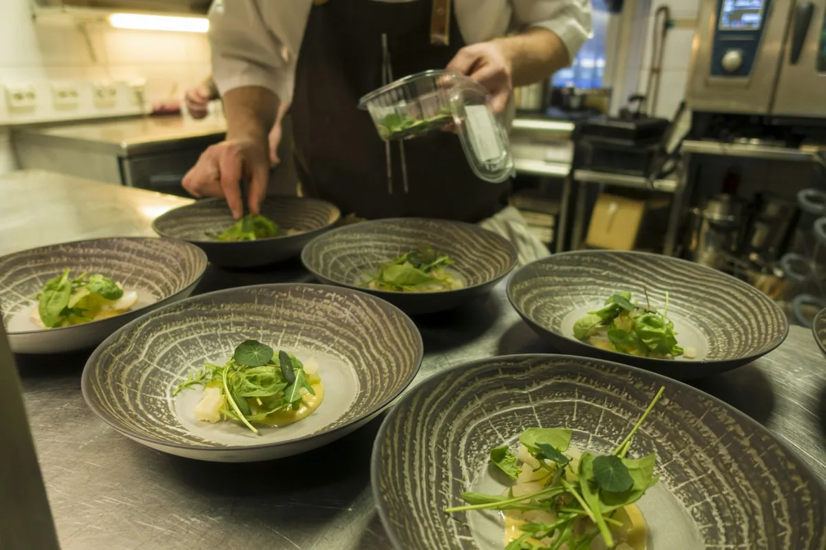 A chef adding the final touches to a row of identically plated starters in a restaurant kitchen