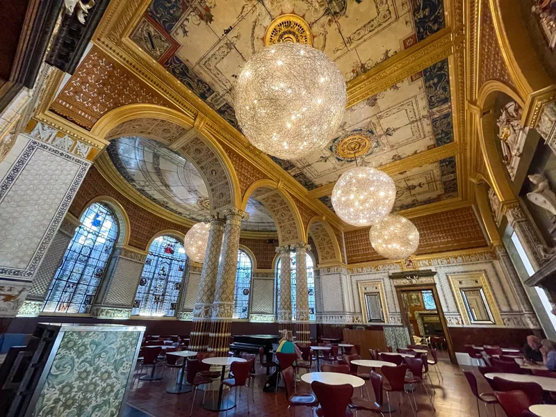 The gilded Gamble Room of the V&A cafe in London, with globe lights hanging above cafe tables