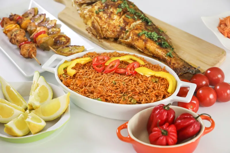 Jollof rice served with a whole fried fish, meat skewers, fried plantain and scotch bonnet peppers