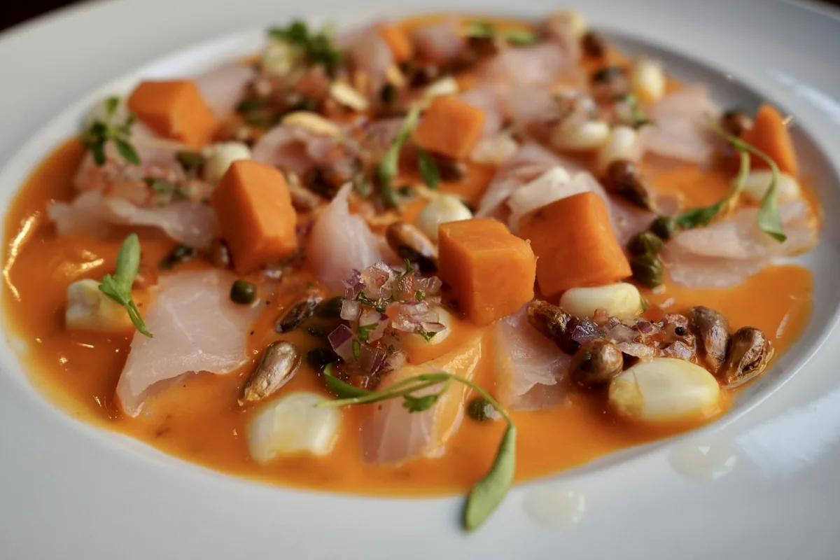 Ceviche of raw white fish with sweet potato, choclo corn and toasted cancha in a pale orange sauce
