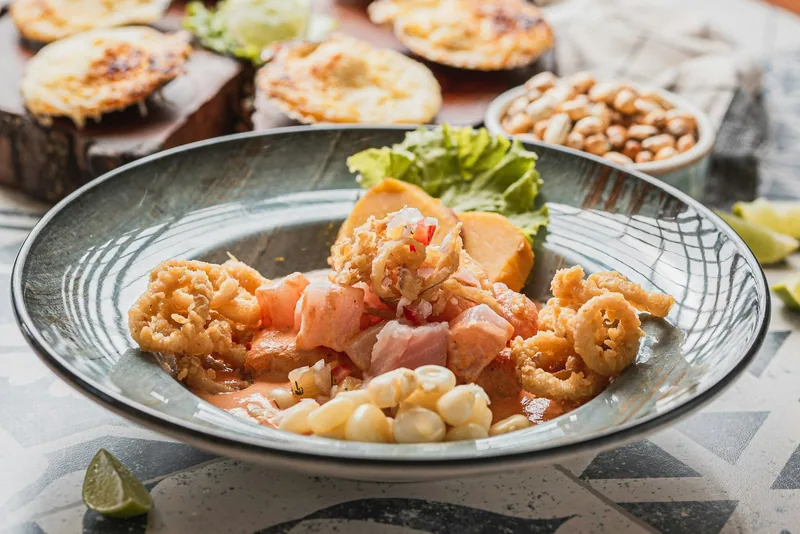 A bowl of ceviche with crisp fried calamari, choclo corn and sweet potato, grilled scallops behind