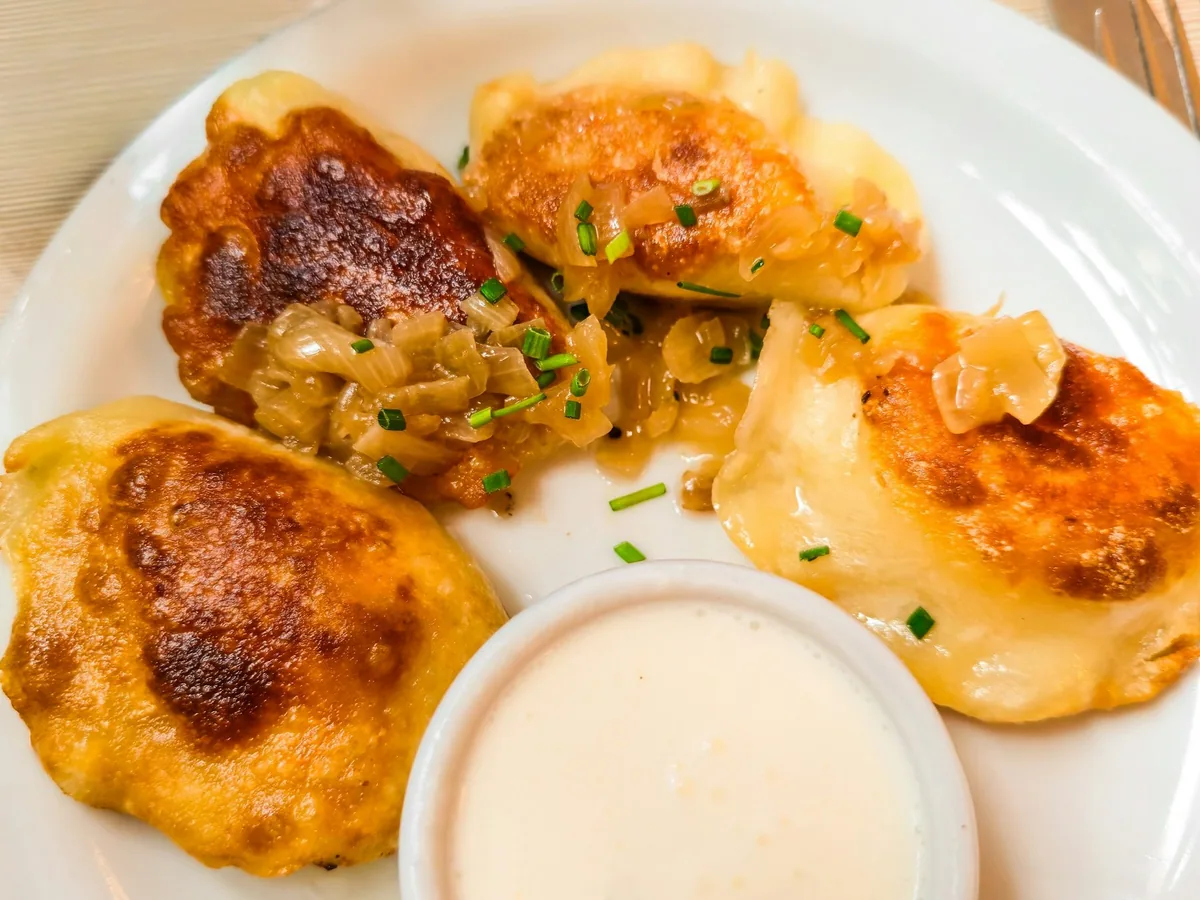 Pan-fried pierogi topped with caramelised onions and chives, with a small bowl of sour cream