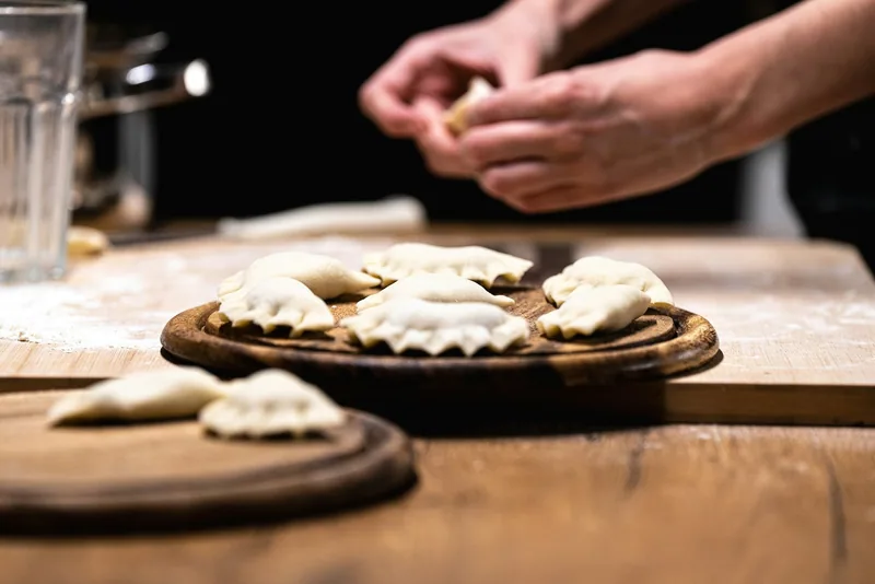 Hands folding raw dumplings on a floured wooden board