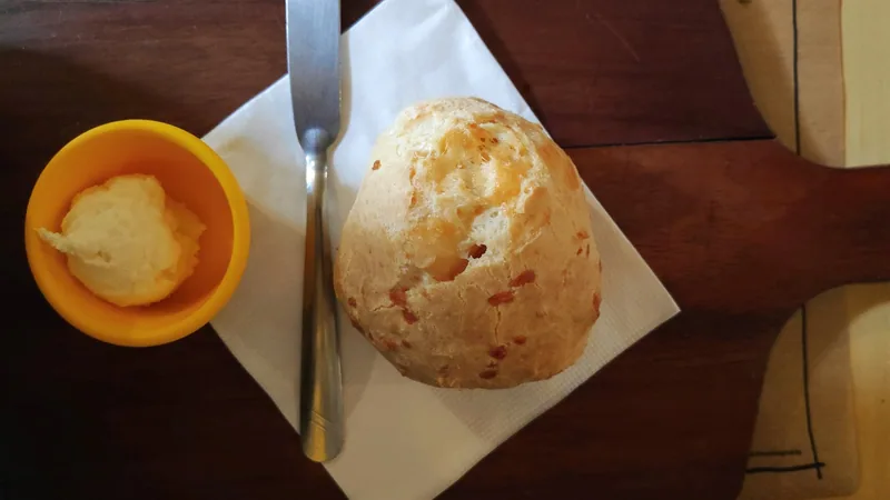 A warm pao de queijo, Brazilian cheese bread, on a napkin beside a small pot of butter