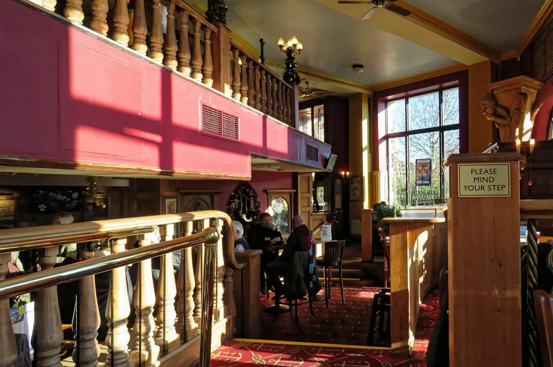 The galleried interior of a City of London pub, with brass rails, patterned carpet and a raised balcony