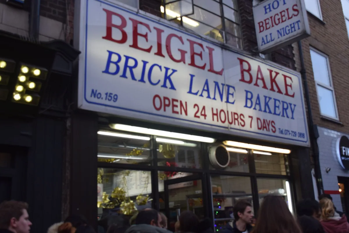 The Beigel Bake shopfront on Brick Lane, its sign promising hot beigels all night, with customers outside