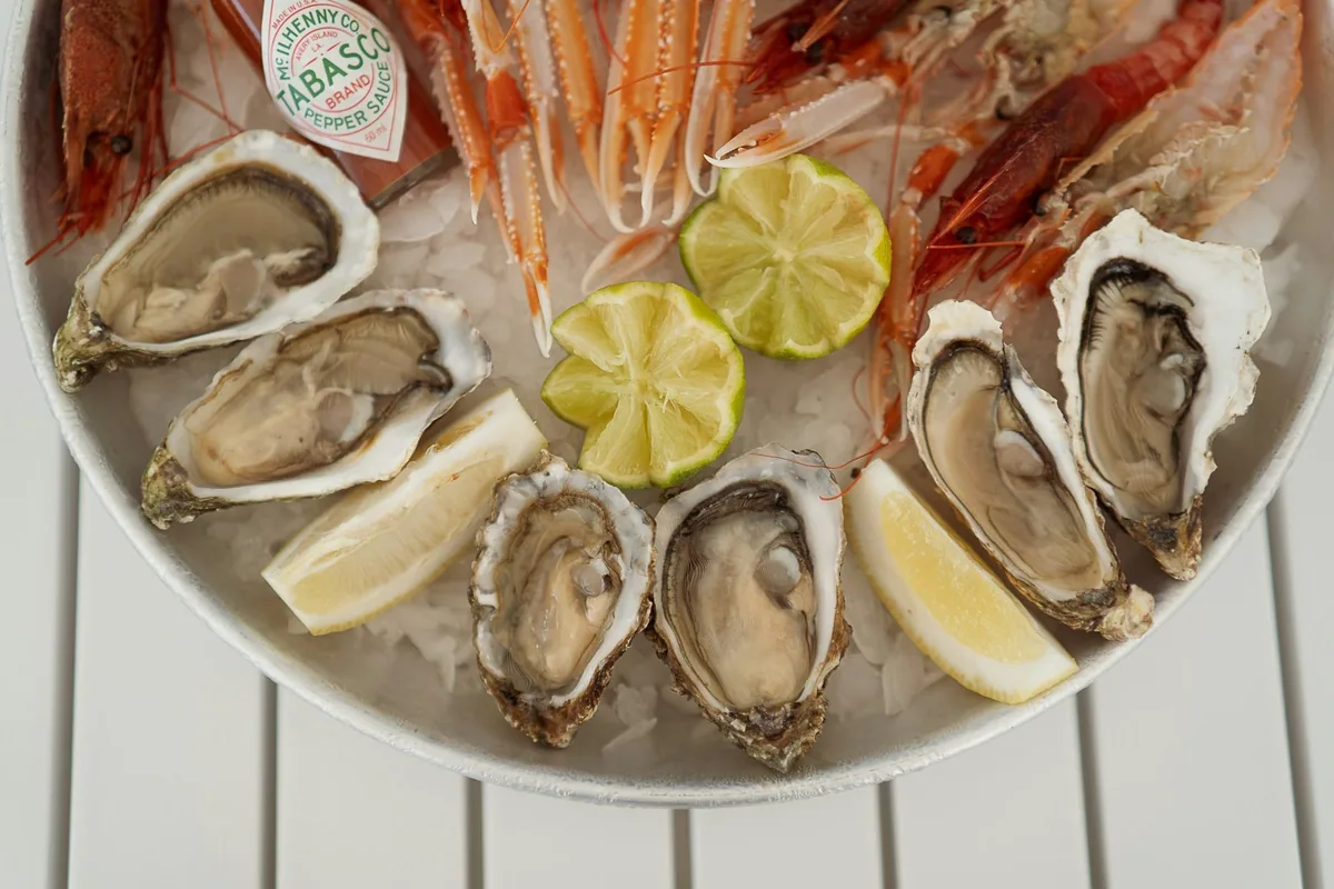 A silver platter of shellfish on ice with oysters, langoustines and lime wedges