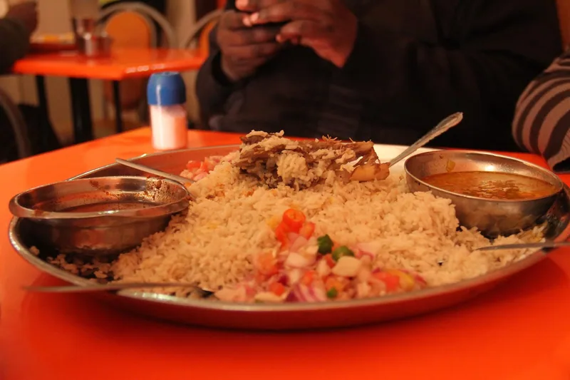 A large steel platter of rice with shredded meat and chopped onion and tomato, two small bowls of sauce beside it, on an orange cafe table