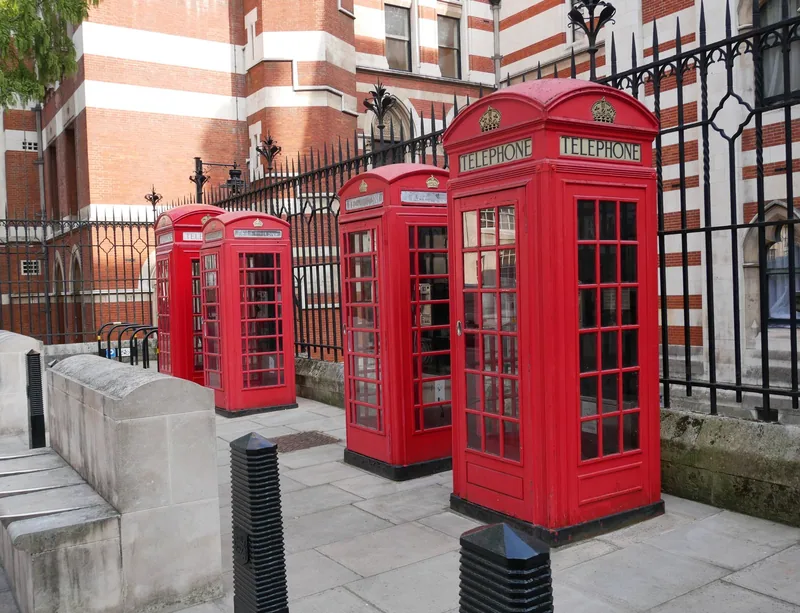 Four red telephone kiosks standing in a row on the Carey Street pavement, against the striped brick and stone flank of the Royal Courts