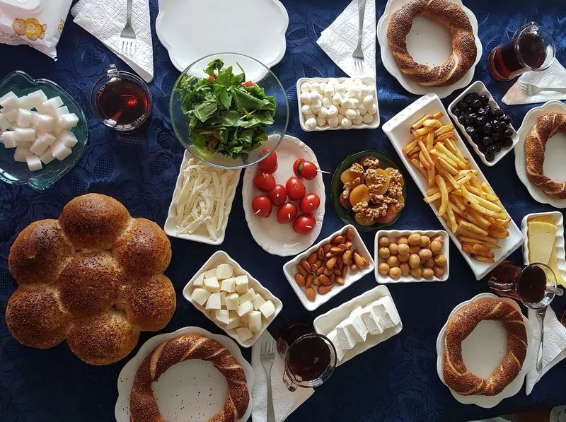 An overhead Turkish breakfast spread of simit, cheeses, olives, tomatoes, jam and glasses of tea