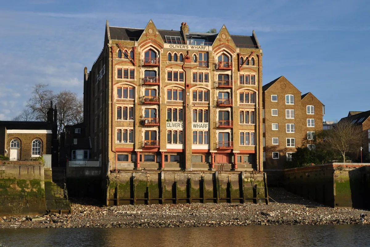 A tall Victorian brick warehouse on the Wapping riverfront, with the gravel foreshore of the Thames exposed below it at low tide