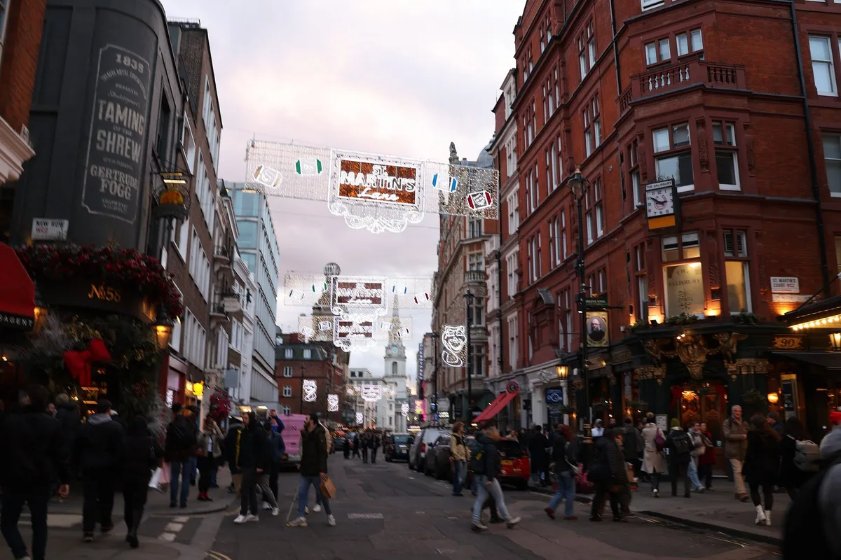St Martin's Lane at dusk with Christmas lights, lit pubs and people on the pavement