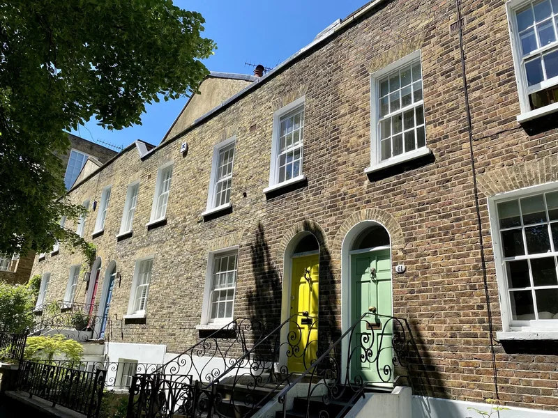 A brick Georgian terrace on Flask Walk in Hampstead, with iron railings and brightly painted front doors up short flights of steps