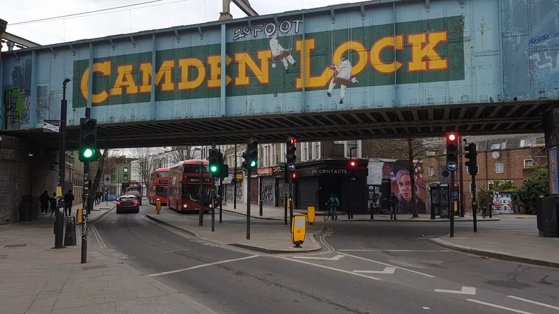 The painted Camden Lock railway bridge over Chalk Farm Road with a red bus passing