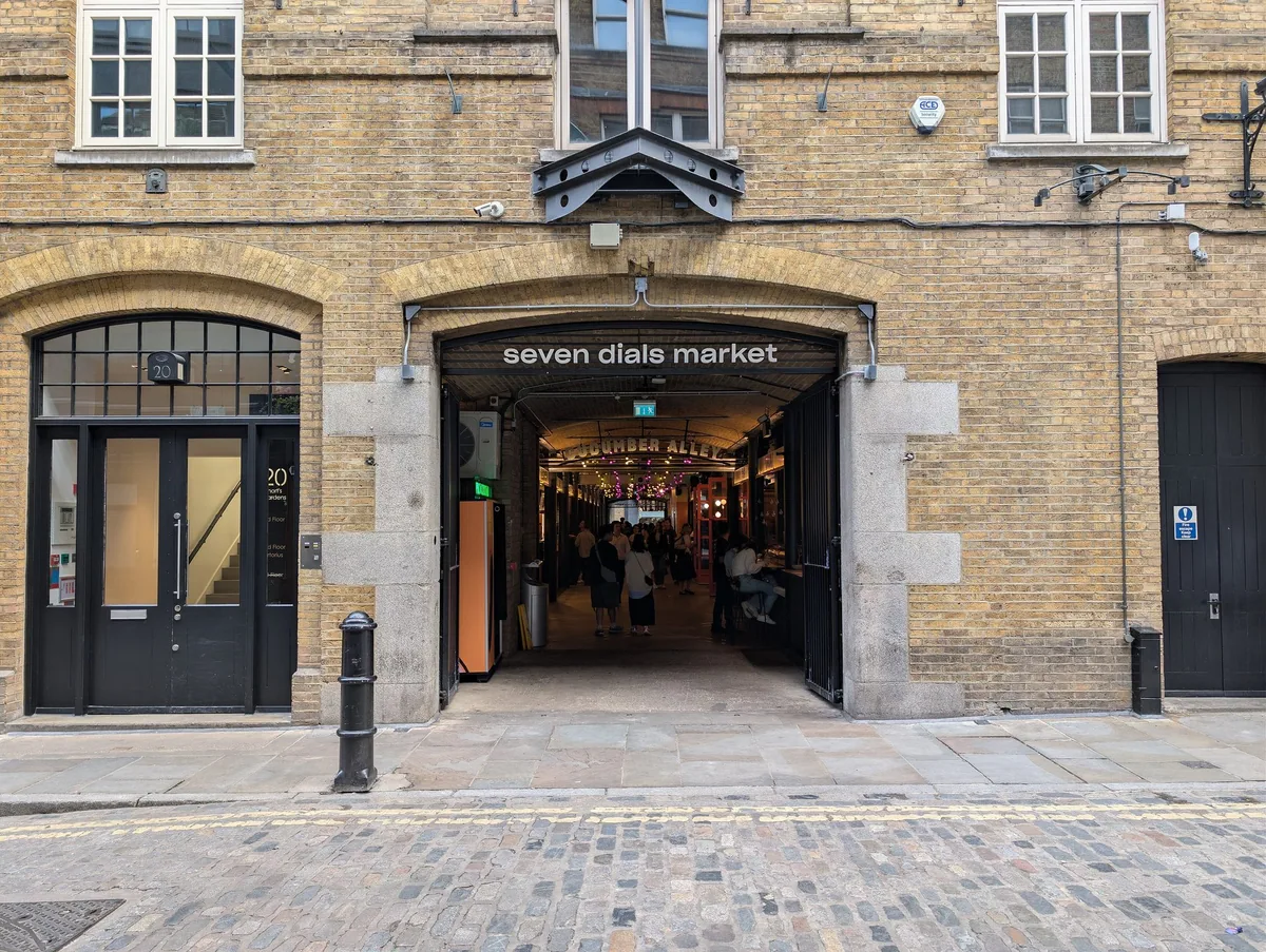 The brick street entrance to Seven Dials Market, with the sign over the archway and Cucumber Alley running inside