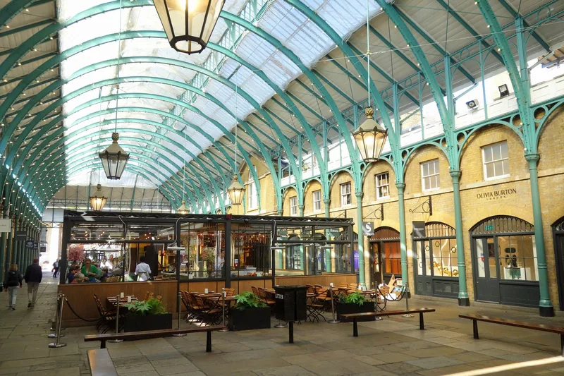 The glass and green ironwork roof of Covent Garden's covered market hall, with cafe tables under the arcade