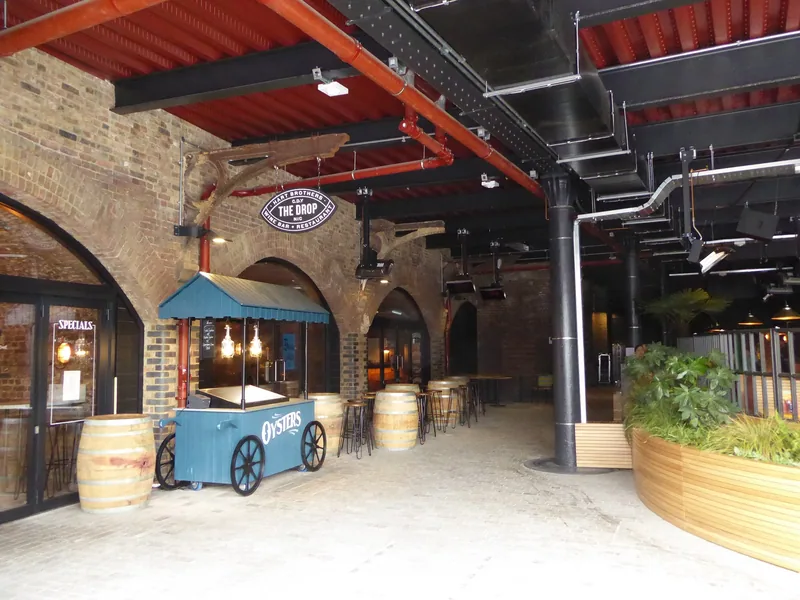 Covered arcade under the brick railway arches at Coal Drops Yard, with a seafood cart, barrels and bar stools