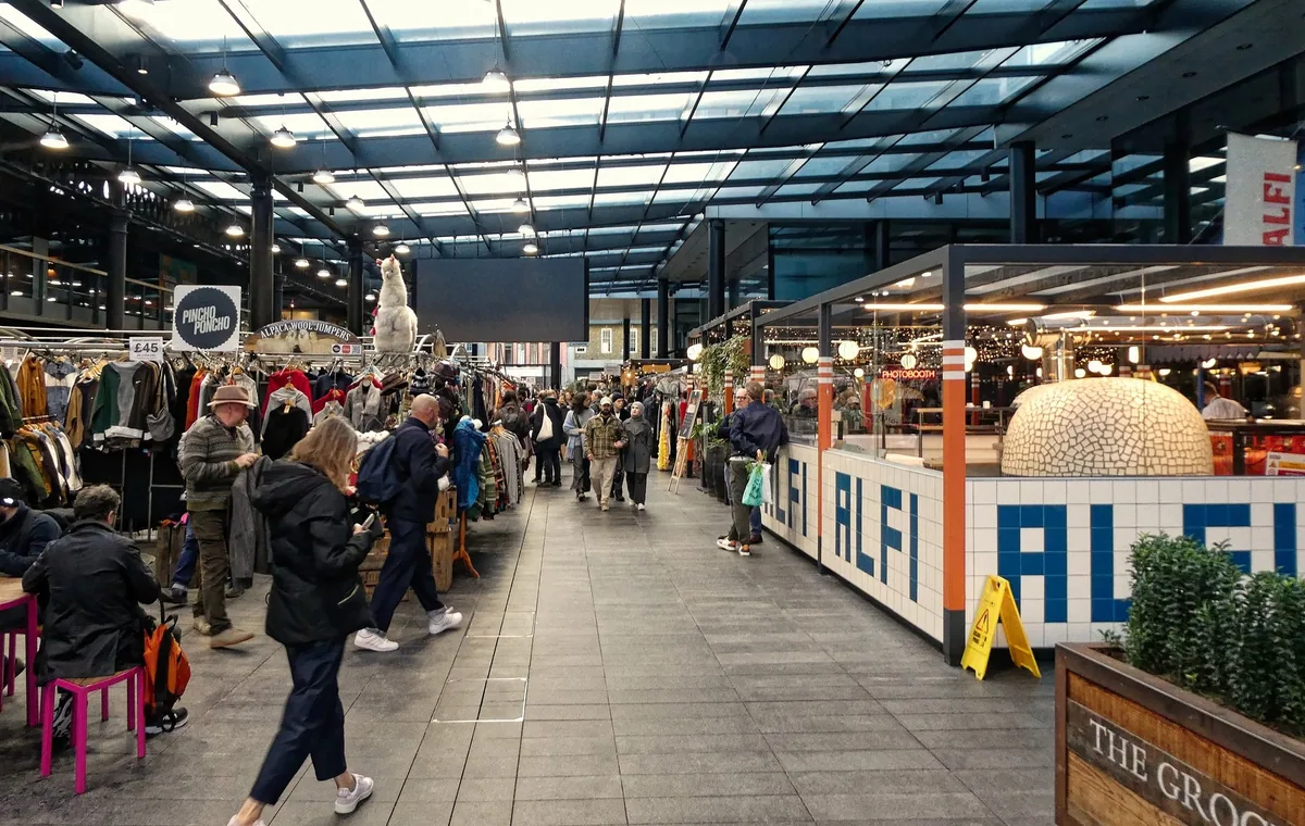 Inside Old Spitalfields Market, with stalls on the left and a pizza counter on the right