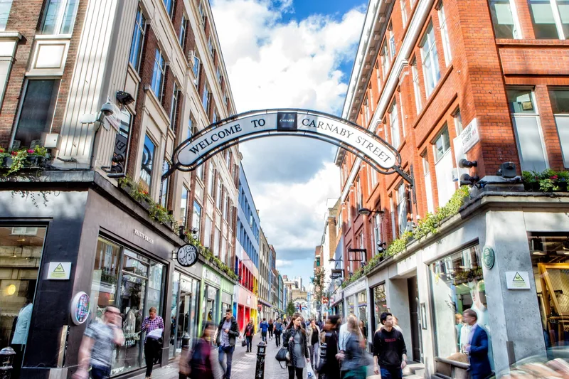 The Welcome to Carnaby Street arch above the pedestrian street, with shoppers passing shopfronts on both sides