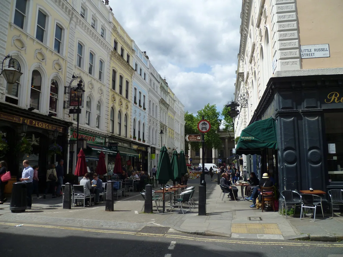 Museum Street at the corner of Little Russell Street, with pub and cafe tables set out on the pavement