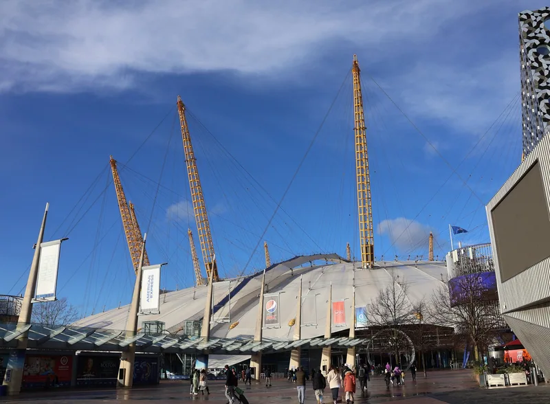 The O2 dome and its yellow masts above the entrance canopy on Peninsula Square, North Greenwich