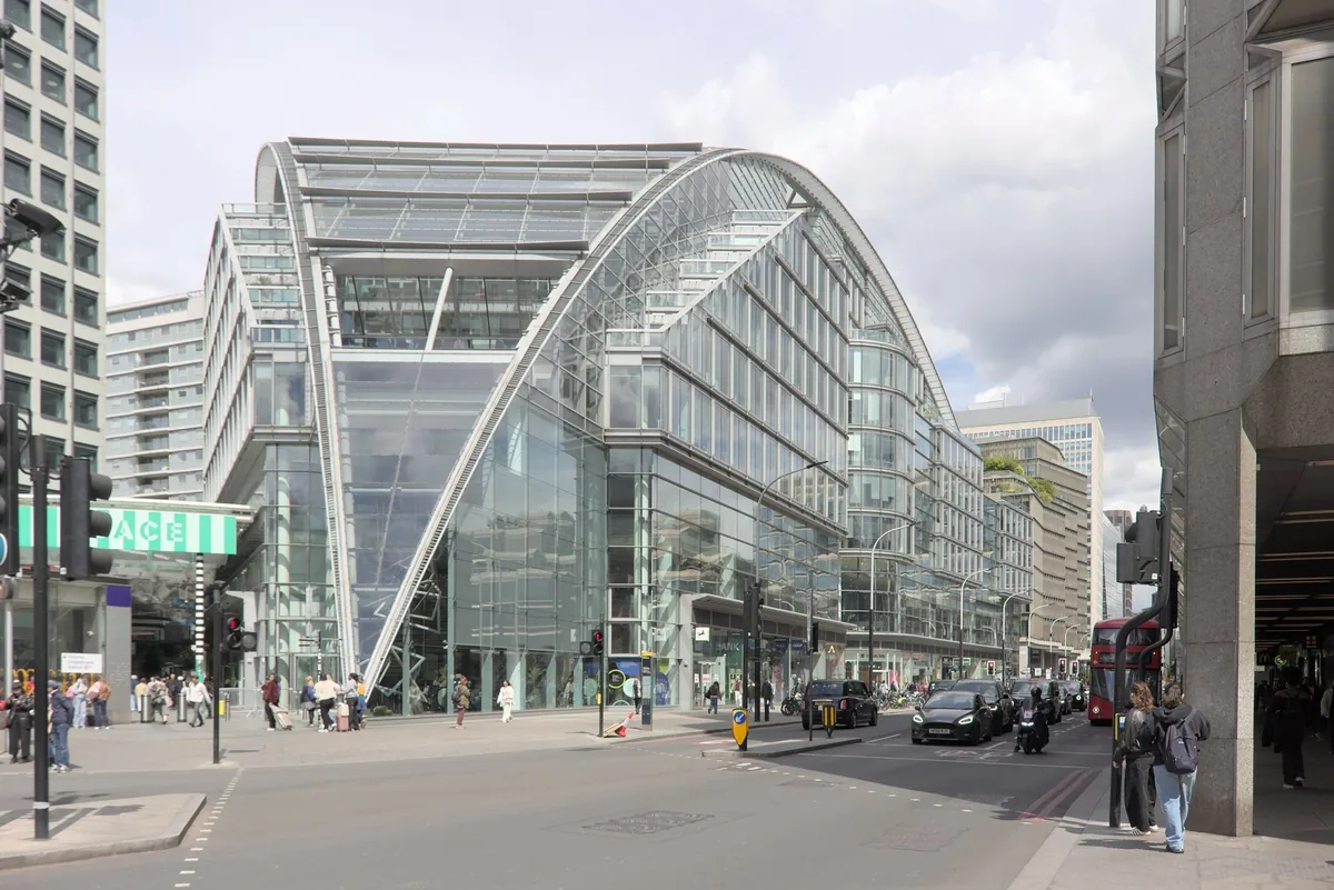 The curved glass roof of Cardinal Place on Victoria Street, with traffic and pedestrians outside the entrance