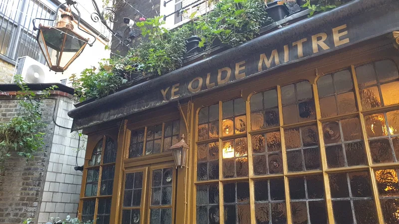 Close view of the pub front: gold lettering reading Ye Olde Mitre above small leaded windows and an ochre painted frame