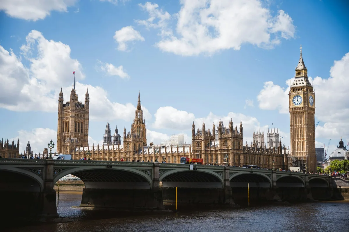 The Houses of Parliament and Big Ben beside Westminster Bridge under a blue sky with white clouds