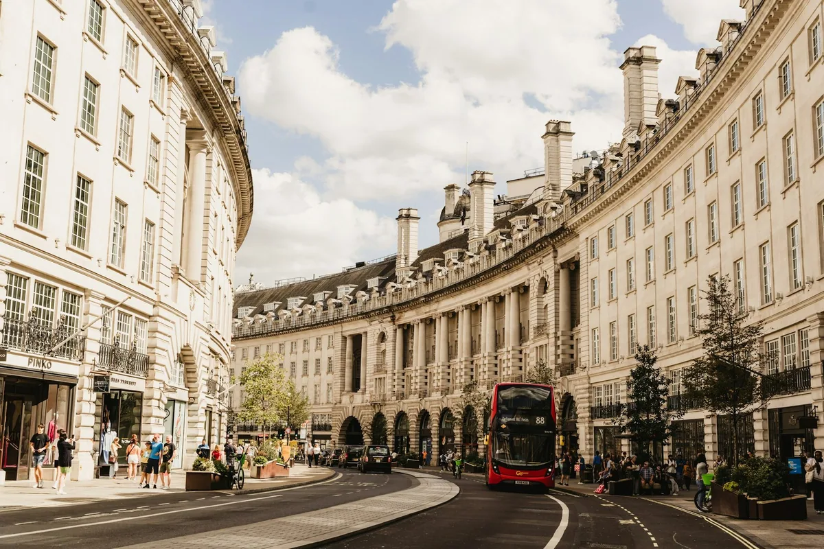 A red double-decker bus on the sweeping curve of Regent Street lined with cream stone buildings