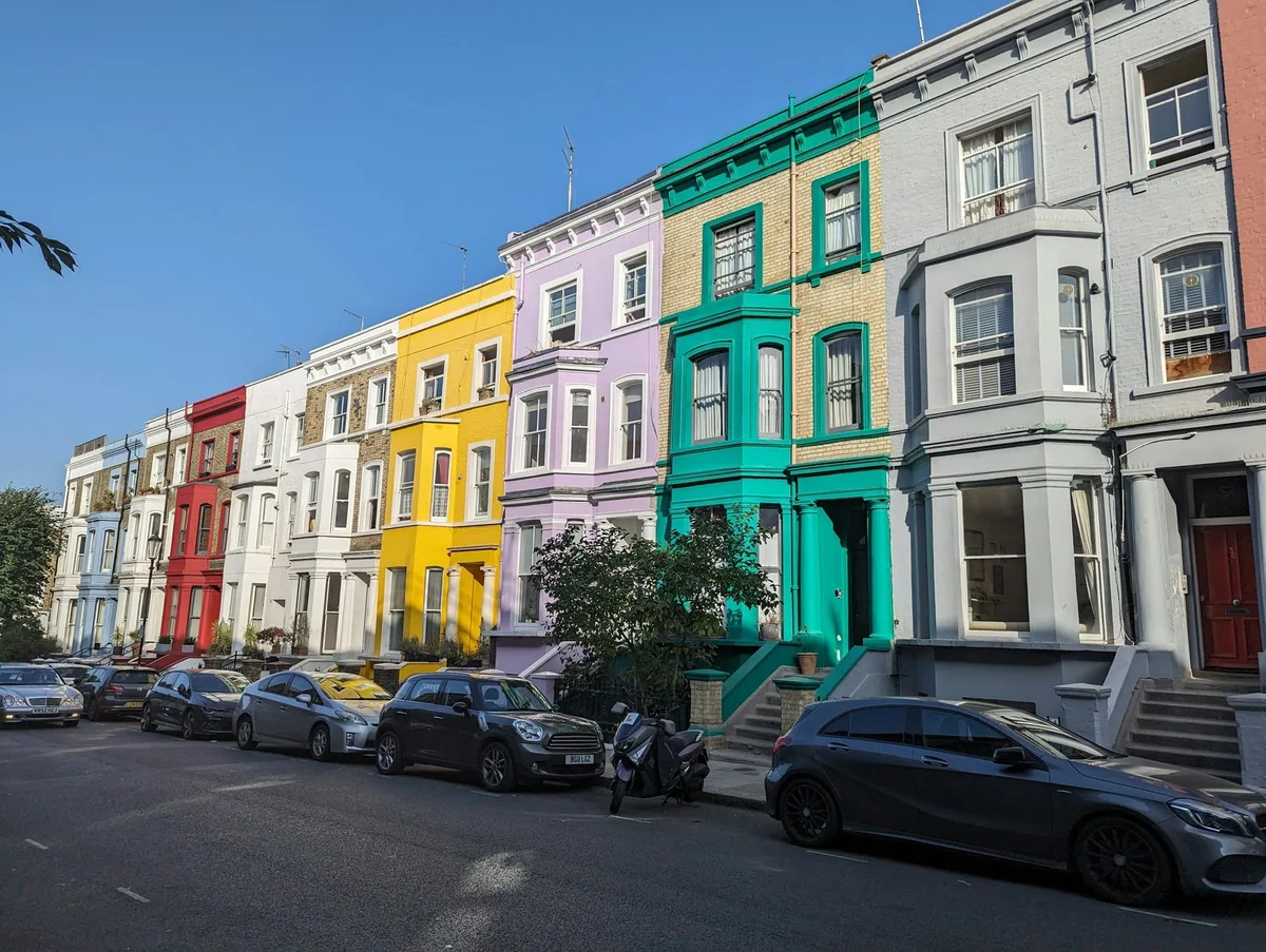 A row of brightly painted terraced houses in yellow, green and blue with parked cars along the street