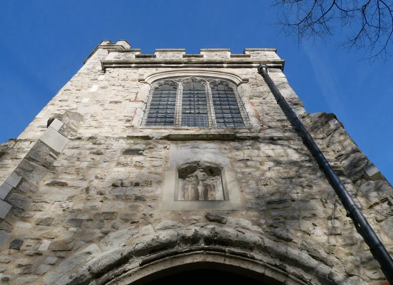 The flint and stone Fire Bell Gate at Barking seen from below, a worn carving set in a niche beneath the traceried window