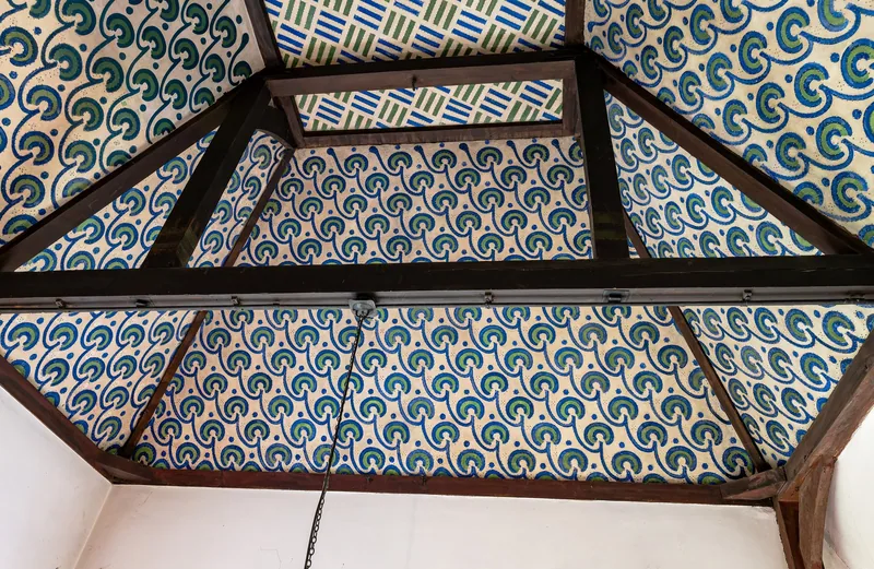 A ceiling at Red House painted in a repeating blue and green pattern between exposed timber beams