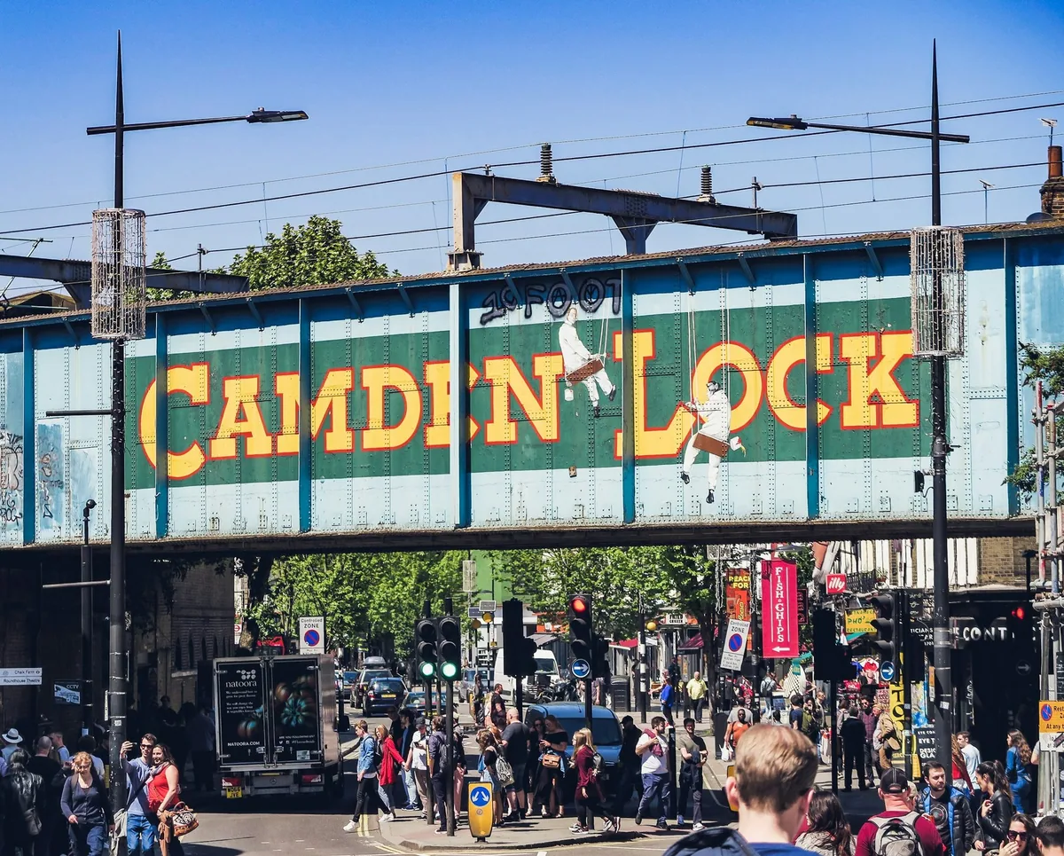 The painted Camden Lock railway bridge spanning the busy street above market crowds