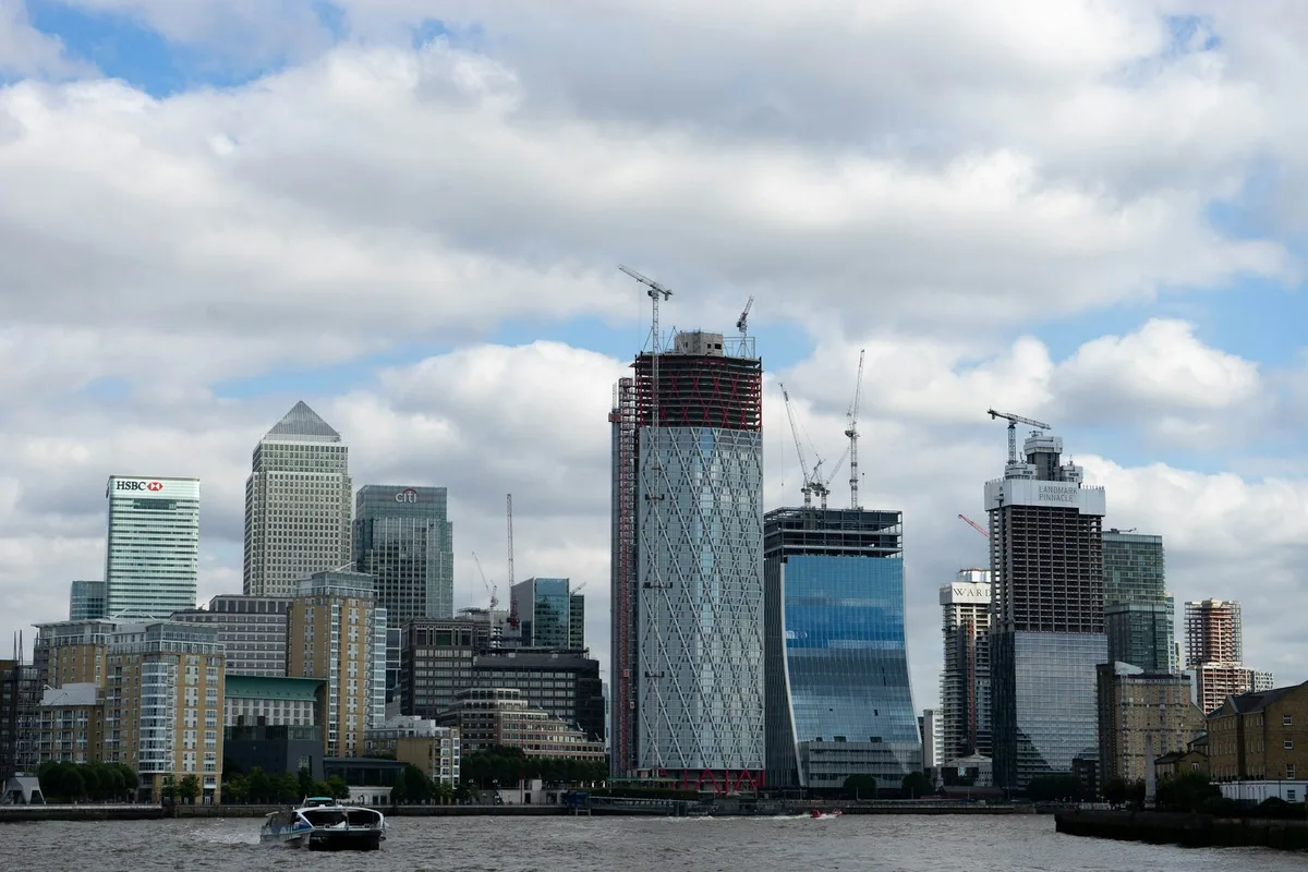 The cluster of Canary Wharf towers seen across the Thames under a cloudy blue sky
