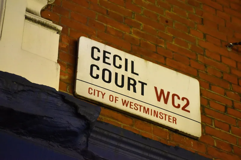 The City of Westminster street sign for Cecil Court WC2, white enamel on a red brick wall above a painted shopfront cornice