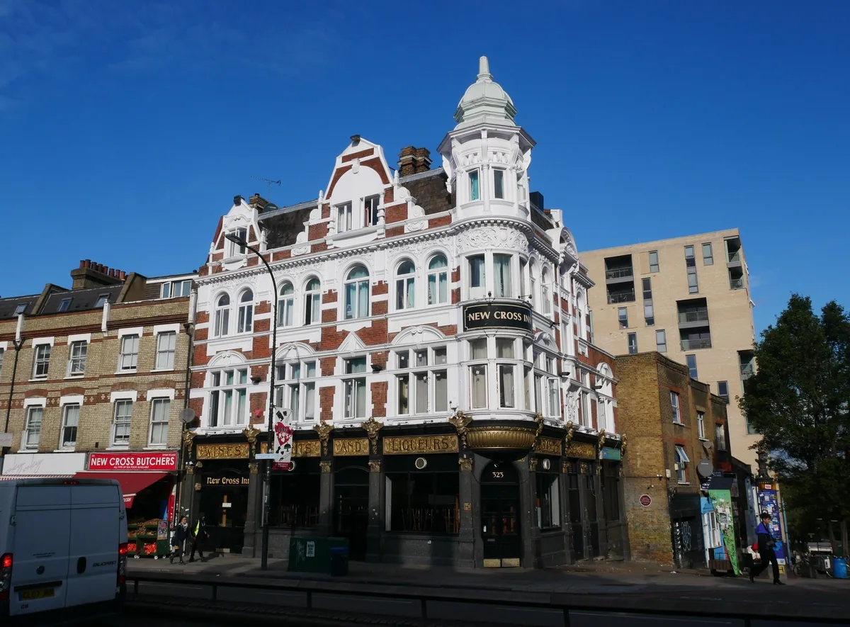 The New Cross Inn, an ornate Victorian corner pub with white gables, under a blue sky