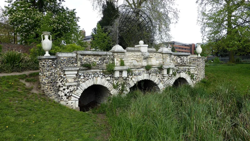 The ornamental stone bridge in Walpole Park, Ealing, set among long grass