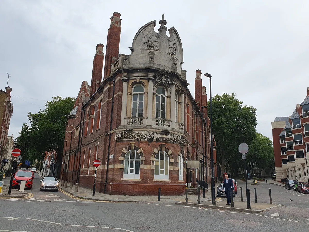 The rounded red-brick and stone corner of Finsbury Town Hall, with its carved frieze and arched windows, seen from Exmouth Market